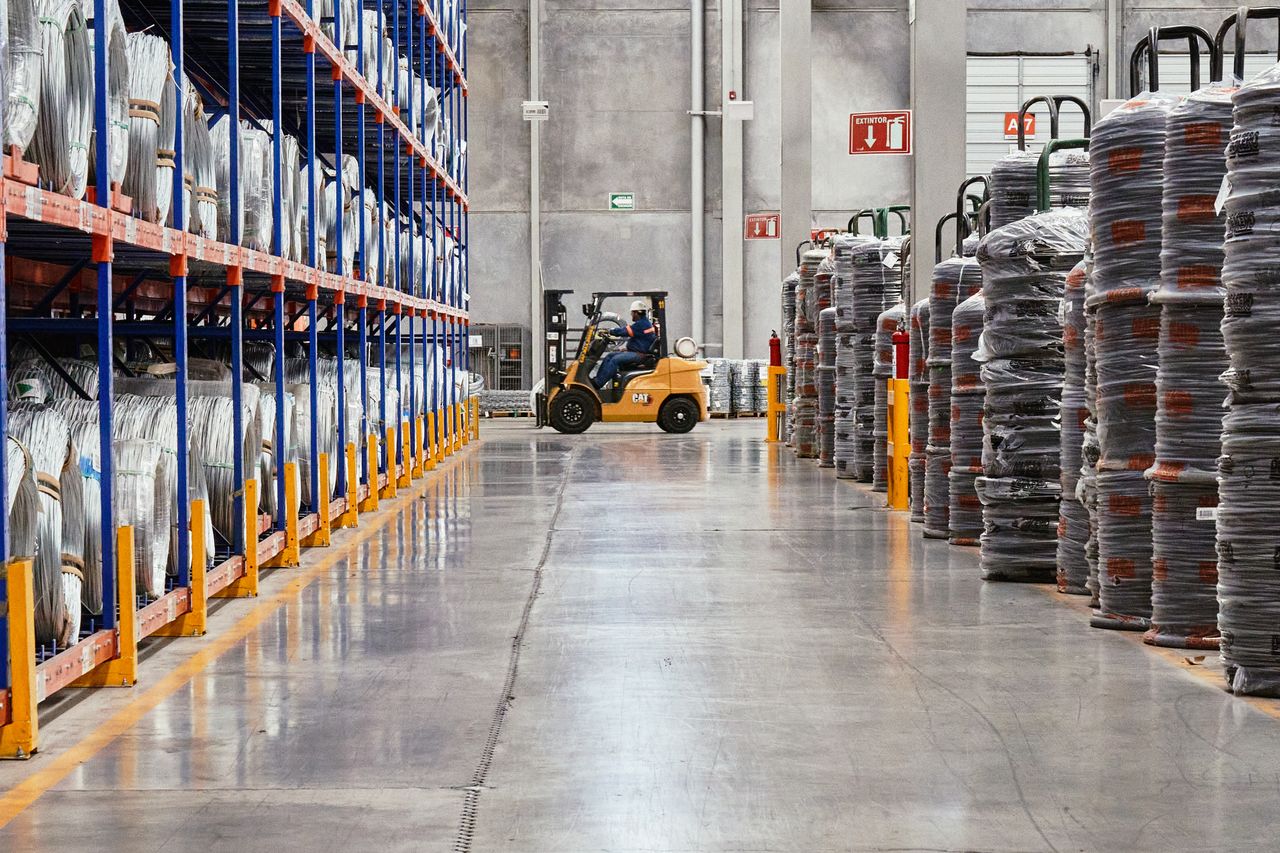 Home A forklift operates in an industrial warehouse with stacked goods. Efficient distribution setting.